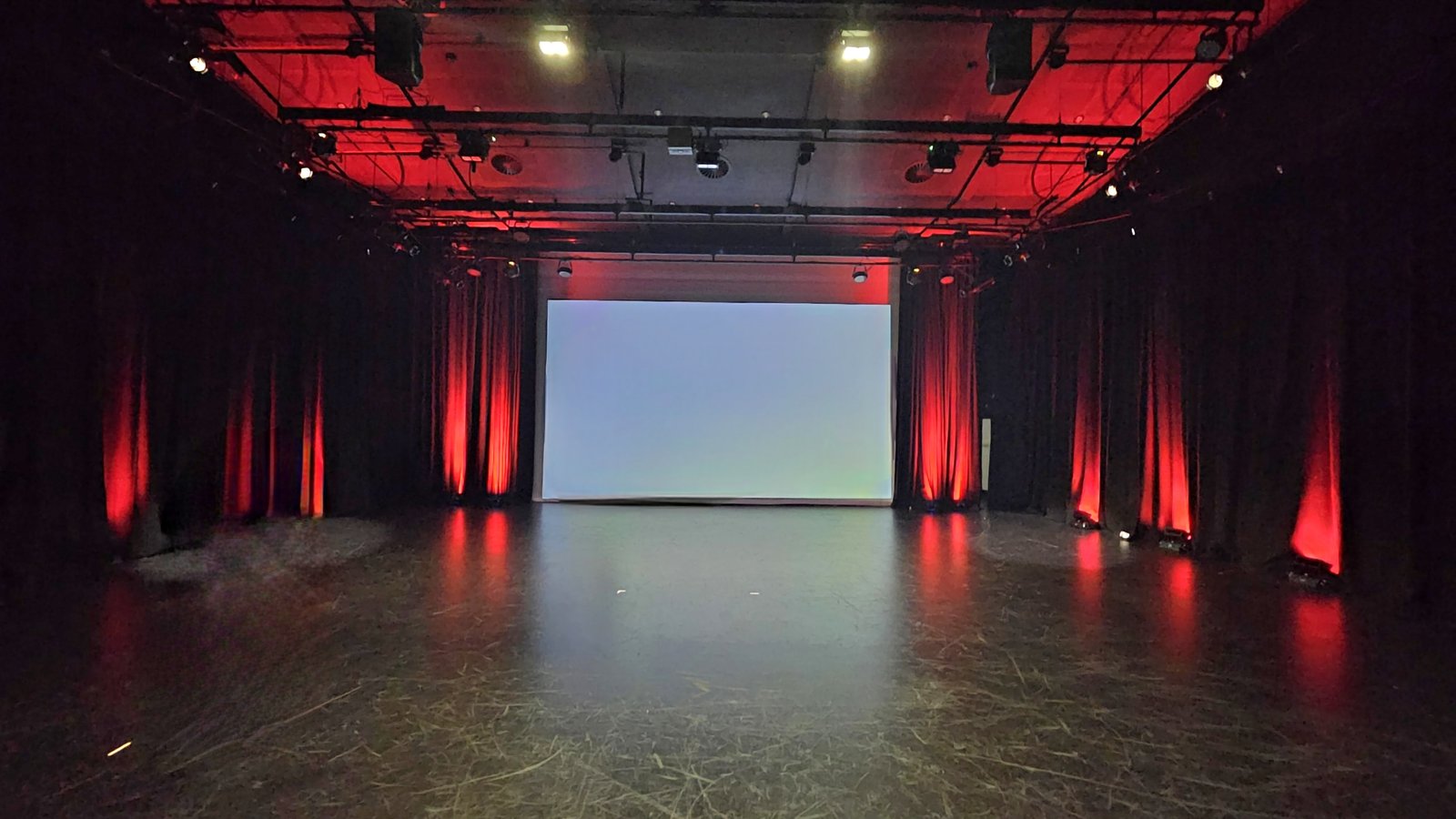 Black box theatre with red stage uplighting and projection screen, Perth school AV by Enchant Entertainment